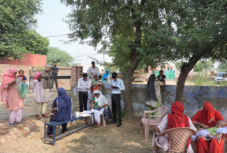 Women with infants wait to see nurse in outdoor courtyard