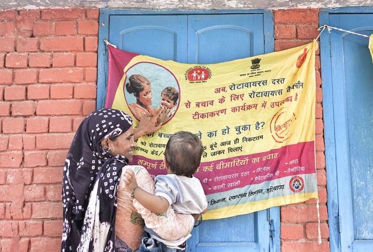 woman holds infant in front of banner advertising vaccines