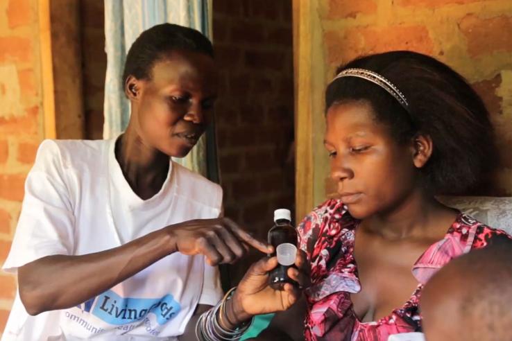 Woman in Living Goods uniform points at medicine bottle while mother of newborn watches