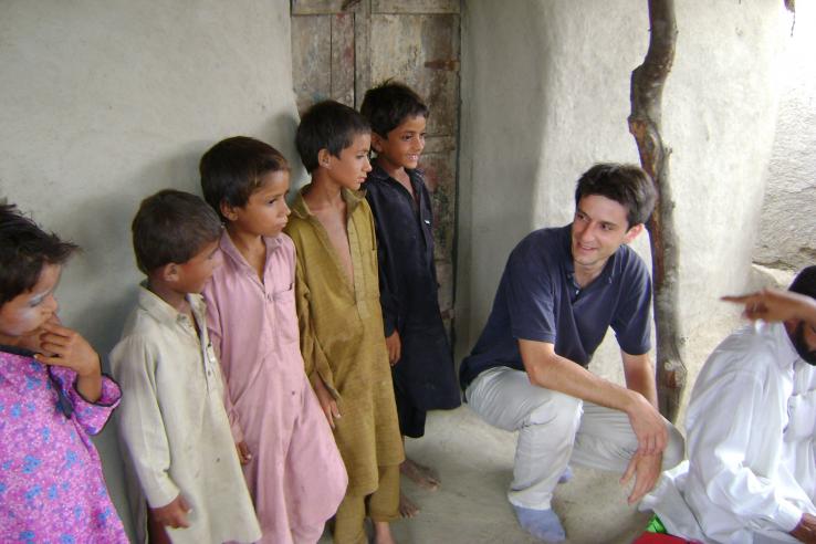 Children in shalwar kameez stand outside of mud building