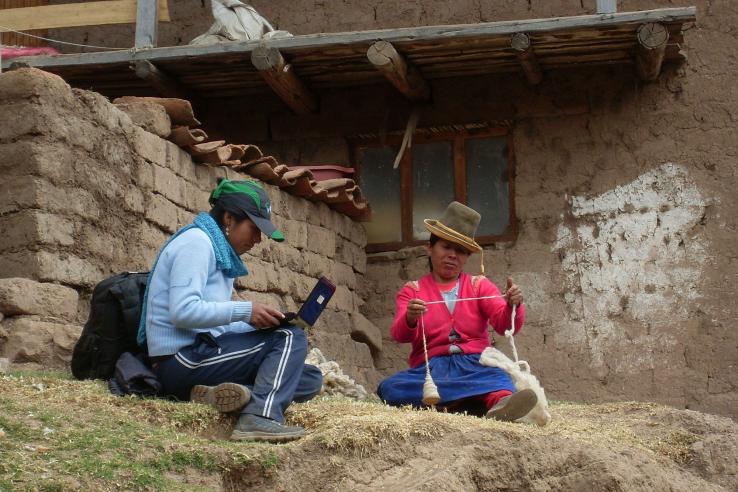 Woman on laptop talks to Peruvian woman spinning wool