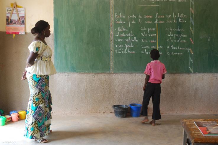 Student practices French grammar exercises on chalkboard as teacher looks on