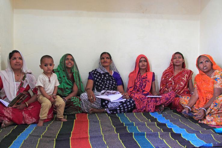 A group of women sit on a rug wearing saris