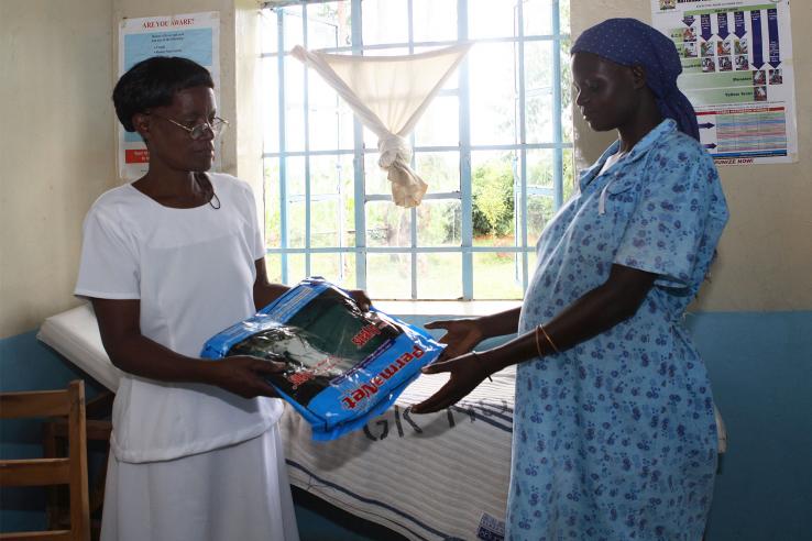A nurse hands a bednet to a pregnant woman