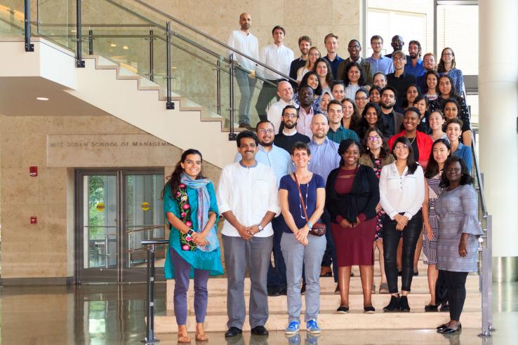 A group of J-PAl staff pose on a stairwell on MIT's campus.