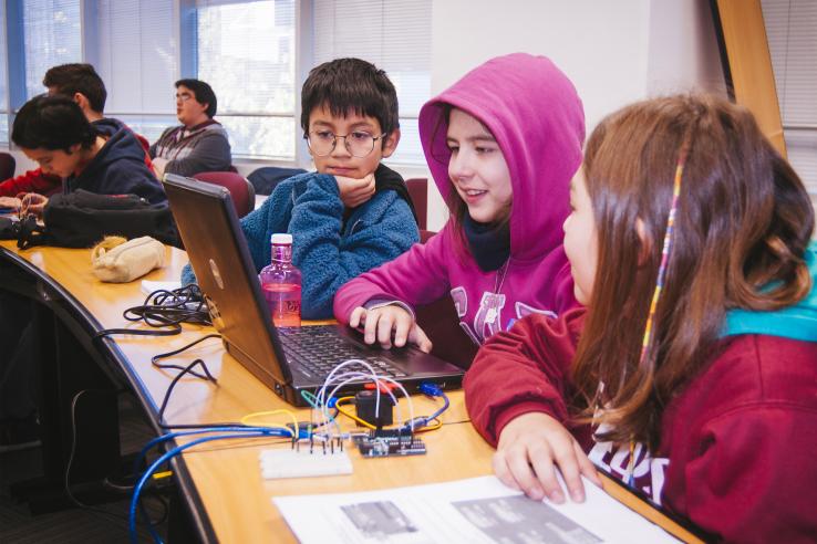 Three students around a computer in a classroom.