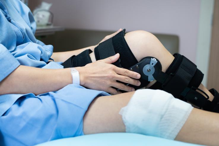 Woman patient with bandage compression knee brace to support injury on hospital bed.
