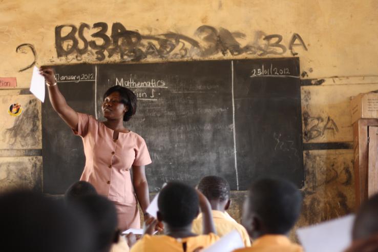 A woman stands in front of a classroom teaching and pointing to a student.