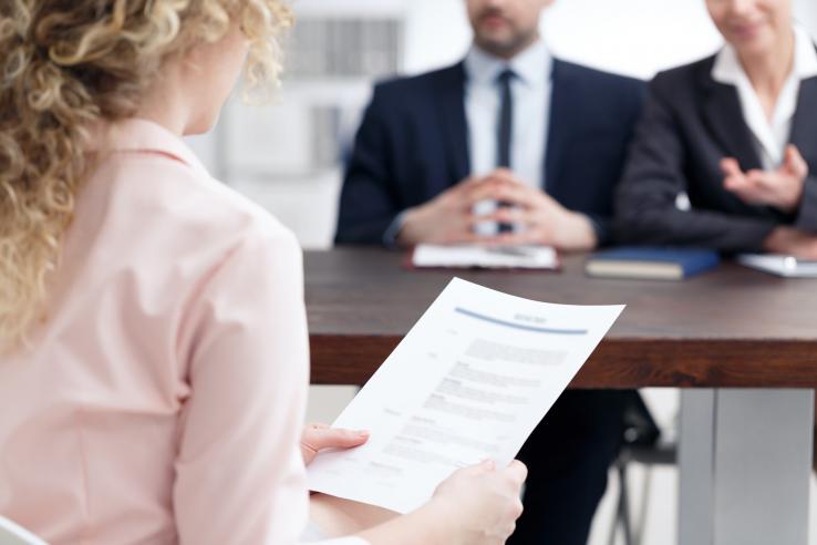 Woman at job interview reading from paper across from two people in suits.