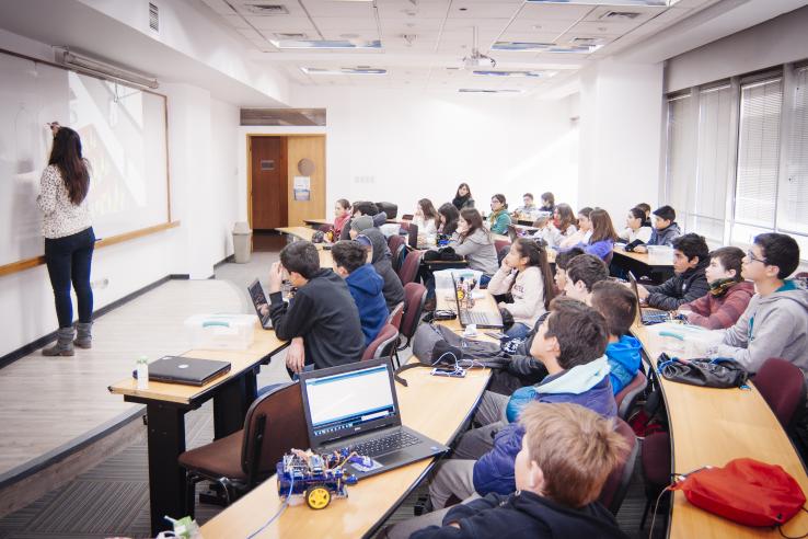 teacher facing a white board and students sitting behind her in a classroom