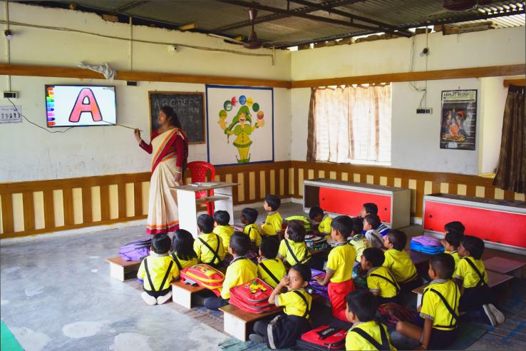 A women teacher is pointing to screen in front of group of young students.