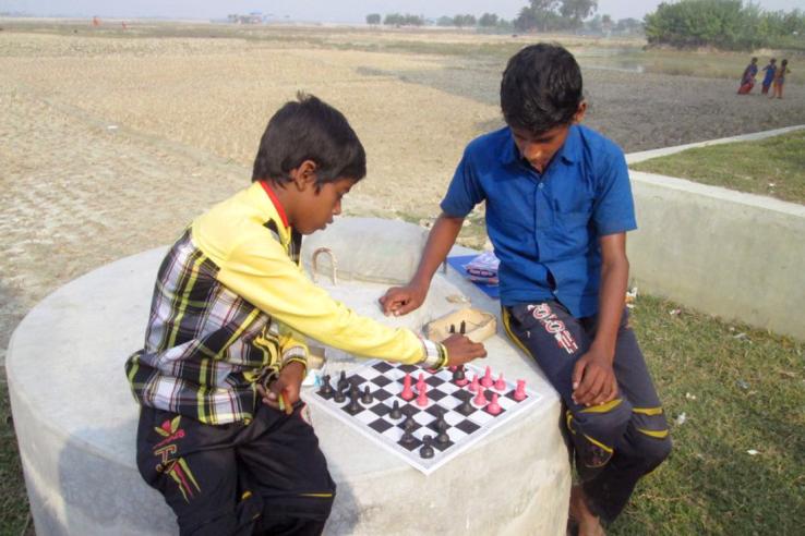 Two boys in rural Bangladesh sit on a large rock in a field playing a game of chess