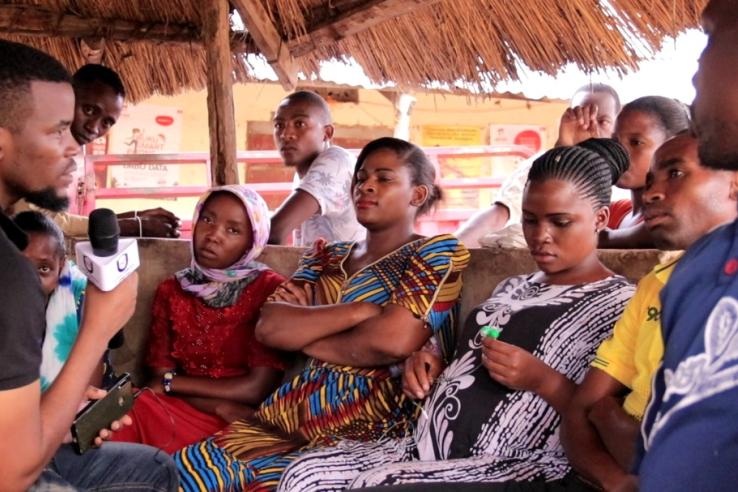 A journalist holding a microphone speaks with community leaders and citizens in Tanzania.