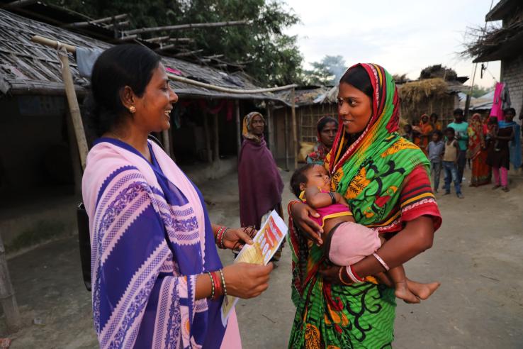 A woman holding a baby speaks to another woman.