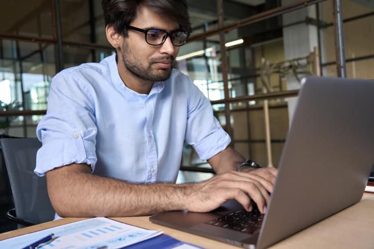 A young Indian employee wearing glasses uses computer working
