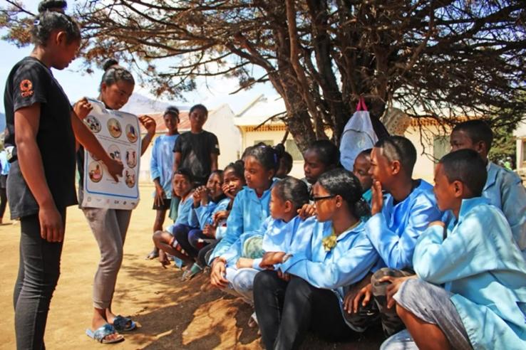 Adolescent girls holding a poster and talking to their classmates about menstruation in Madagascar