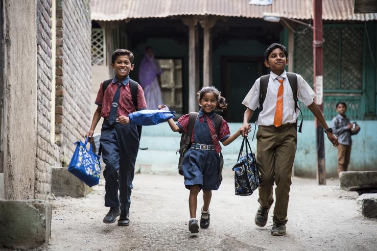 Three schoolchildren walk down a street smiling