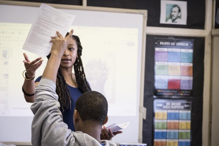 A woman is handing out materials to a student in a classroom.