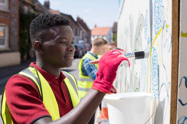Teenage boy in red shirt and yellow vest paints public mural