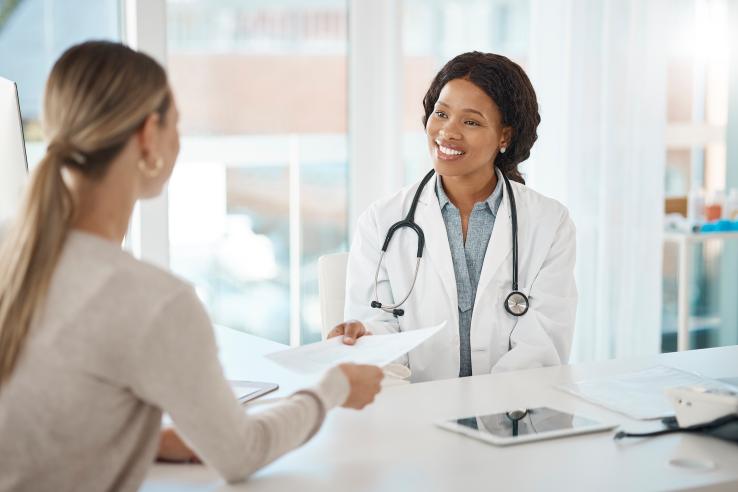 A female black doctor hands blonde woman paper with medical consultation in france