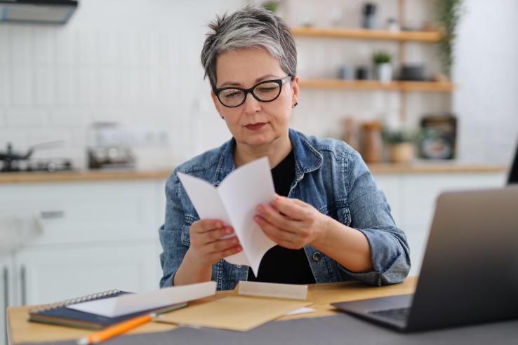 A middle-aged woman with short hair and glasses reads a fundraising letter from a German charity