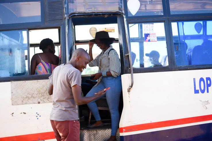 Kenyan man looks at savings tool on his phone as he gets on bus