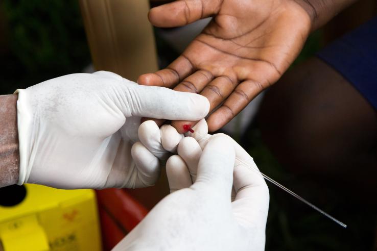 A health worker wearing white gloves doing a finger prick test for HIV