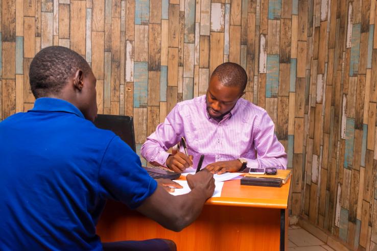 Two male bureaucrats in collard shirts are filling out paperwork about performance
