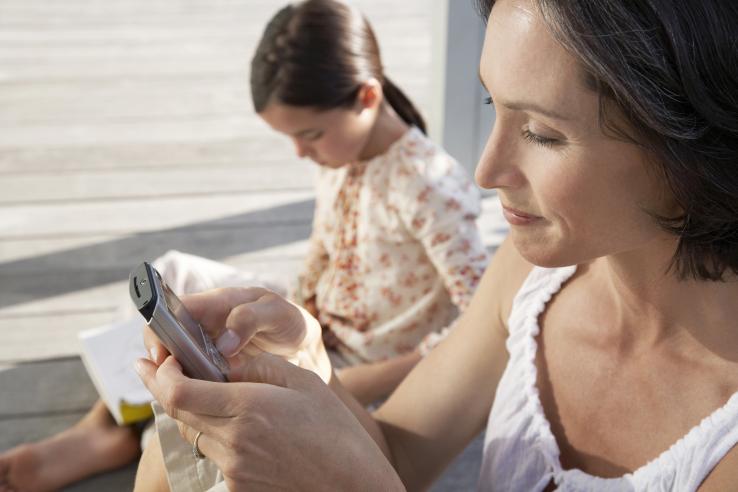 Mother of student checking text message from school with student sitting in background