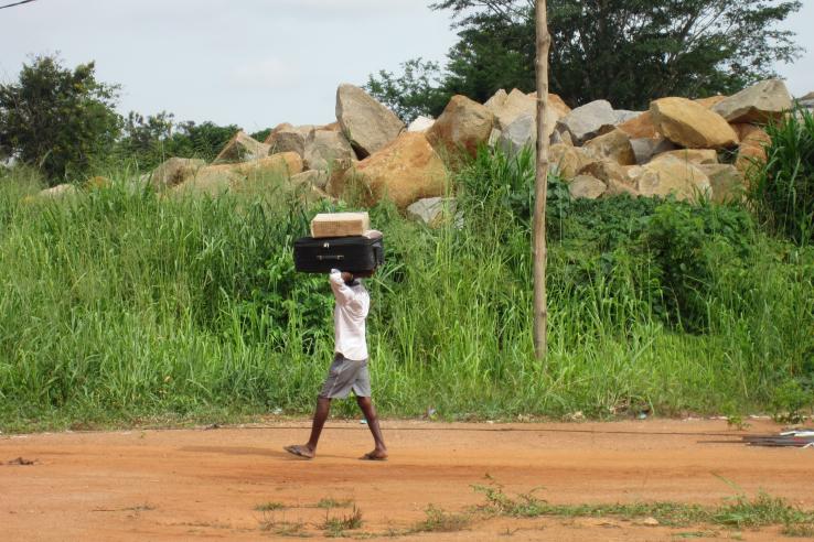 Young boy carrying suitcase on his head walking along a road in Nigeria. 