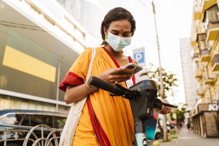 Woman wearing a face mask checks her phone on a city street in India.