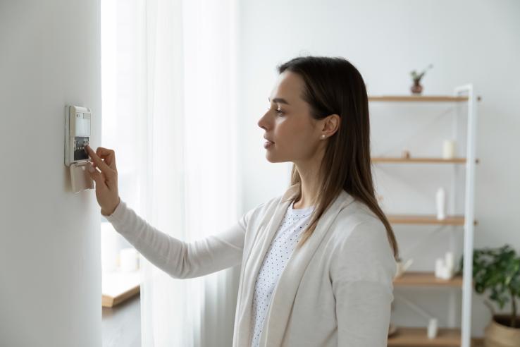 Woman with brown hair monitoring electricity use by checking thermostat in the United States