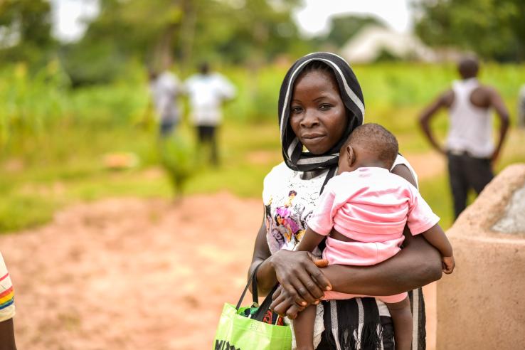 A mother carries her child in her arms outdoors in Nigeria.