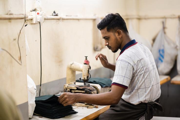 Man works at sewing station with pieces of black leather. 