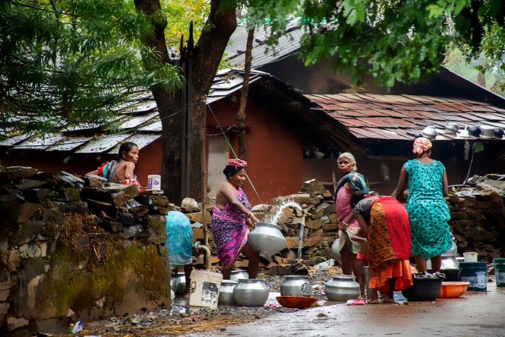  A group of women gather around a roadside tap, filling their containers with water. 