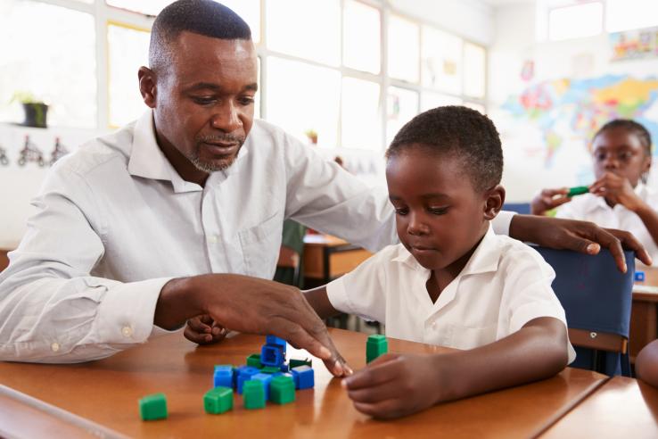 Male teacher using play-based learning with blocks to help elementary school boy count in South Africa