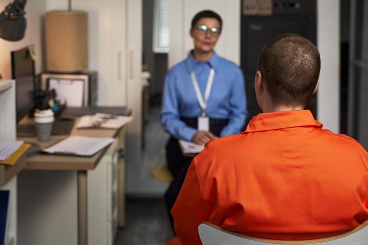 Person in orange jumpsuit sits across from case manager in an office