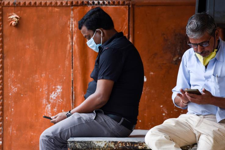 Two men sit on a bench with their phones in their hands