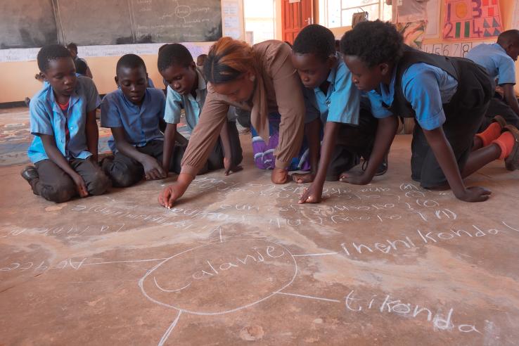 Students squat and write math problems using chalk.