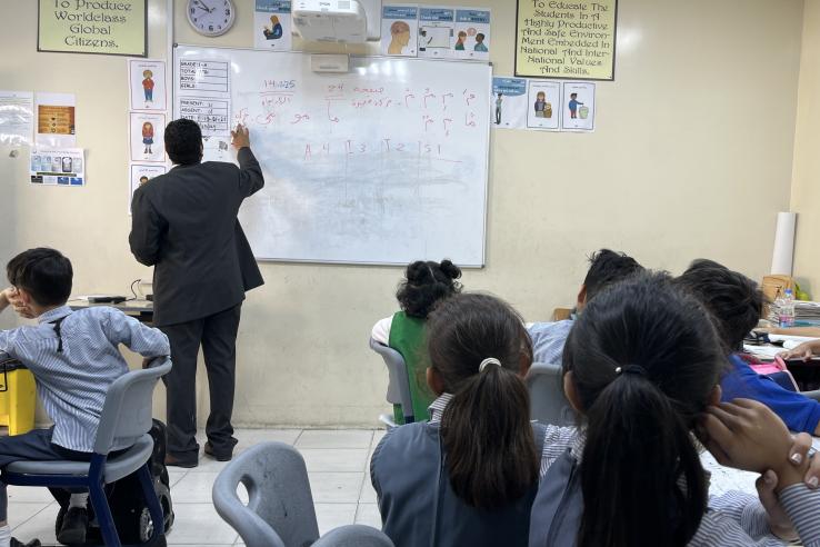A teacher stands with his back to a classroom of students. The teacher is teaching using the Iqra curriculum.