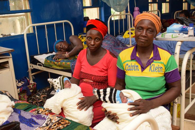 Women sit on a hospital bed holding two infants.