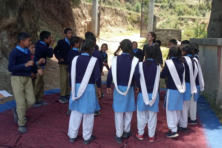 Students standing outside on a rug in a circle around a teacher