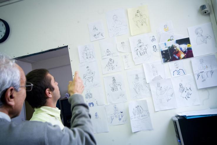 Young man and older man look at drawings taped to wall