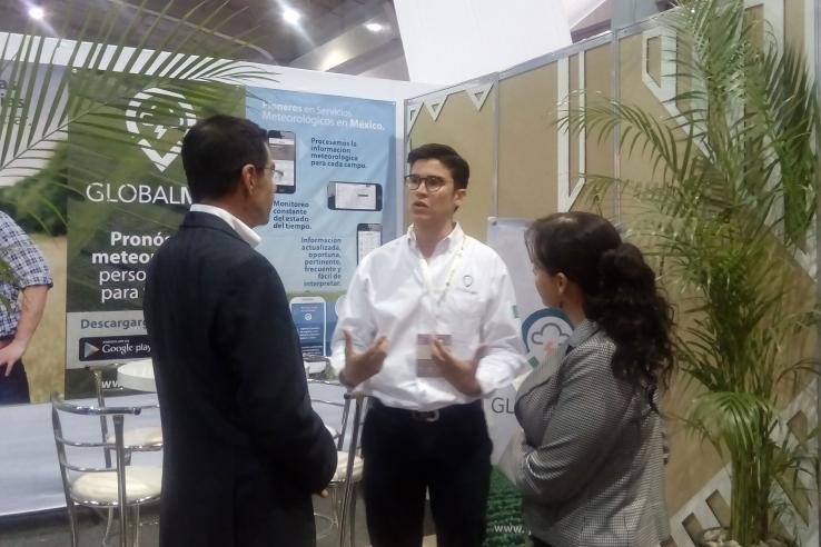 Man speaks to two judges in front of a booth with promotional materials for Globalmet