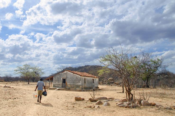 Man carries buckets of water to house in dry landscape