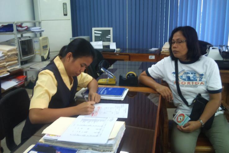 Woman writes on papers while woman looks on from across the desk