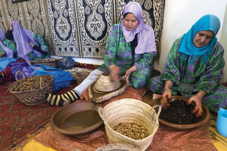 Women in headscarves seated on moroccan rugs process seeds