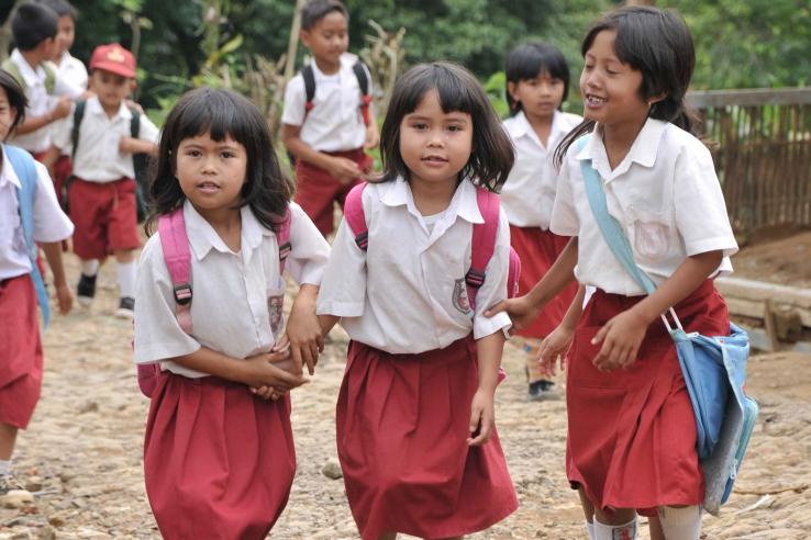 Three girls in uniforms with backpacks walk outside