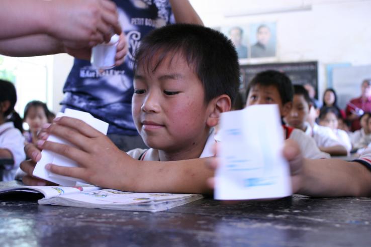 Chinese child seated at desk holds open white packet