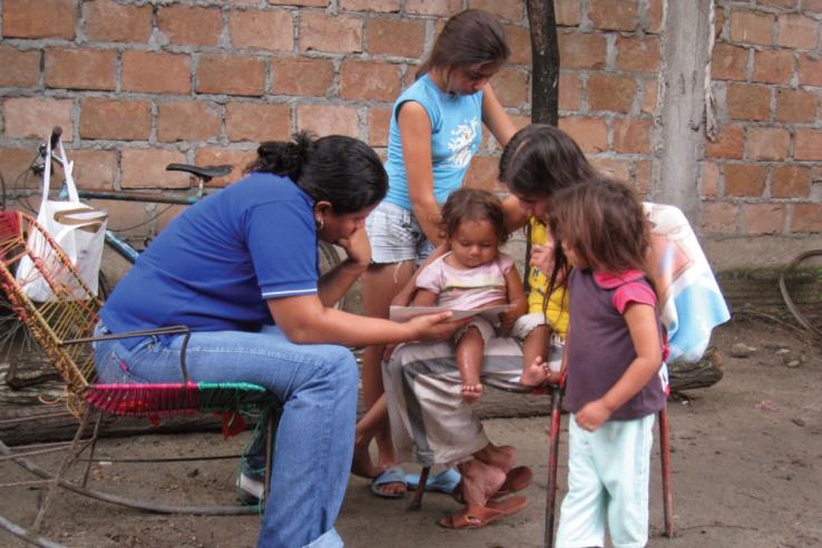 Two adult women sitting in chairs reading with three children.